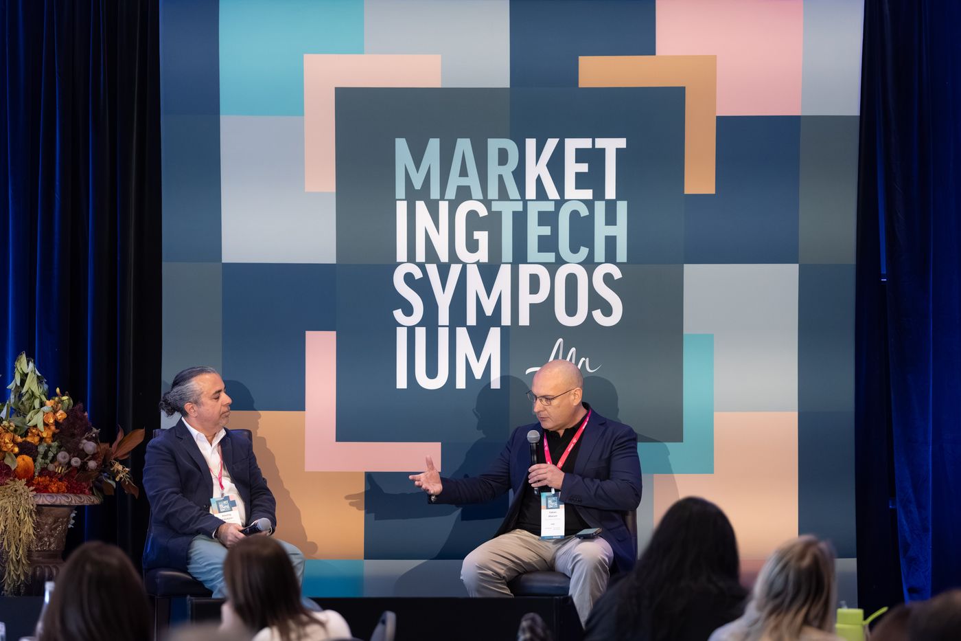 Khachig Kabakjian and Fabian Abacum seated on stage in front of the Marketing Tech Symposium backdrop, Fabian speaking