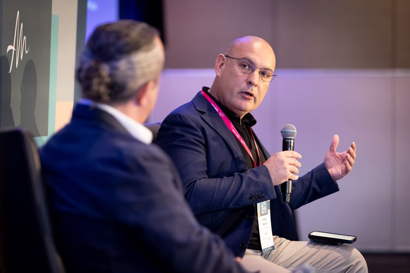 Fabian Abacum answering a question with a microphone, seen past Khachig Kabakjian