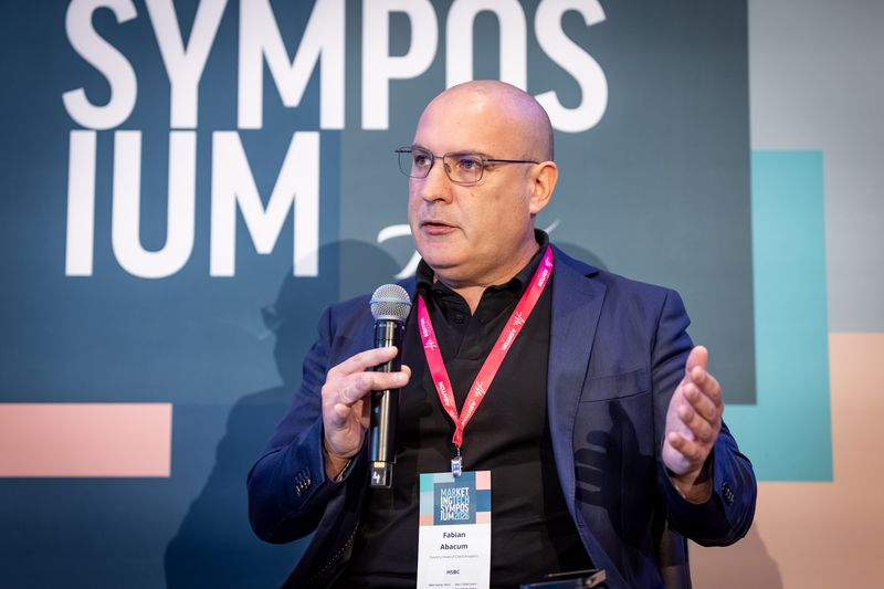 Fabian Abacum presenting in front of the symposium backdrop, wearing his speaker badge
